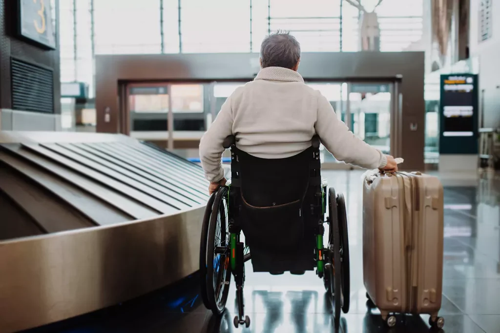 A disabled man sitting in his wheelchair holding his suitcase at the airport