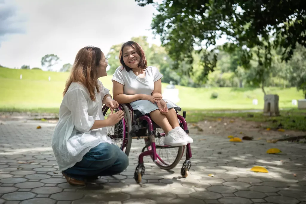 A disabled woman sitting in her wheelchair and her support worker in the park