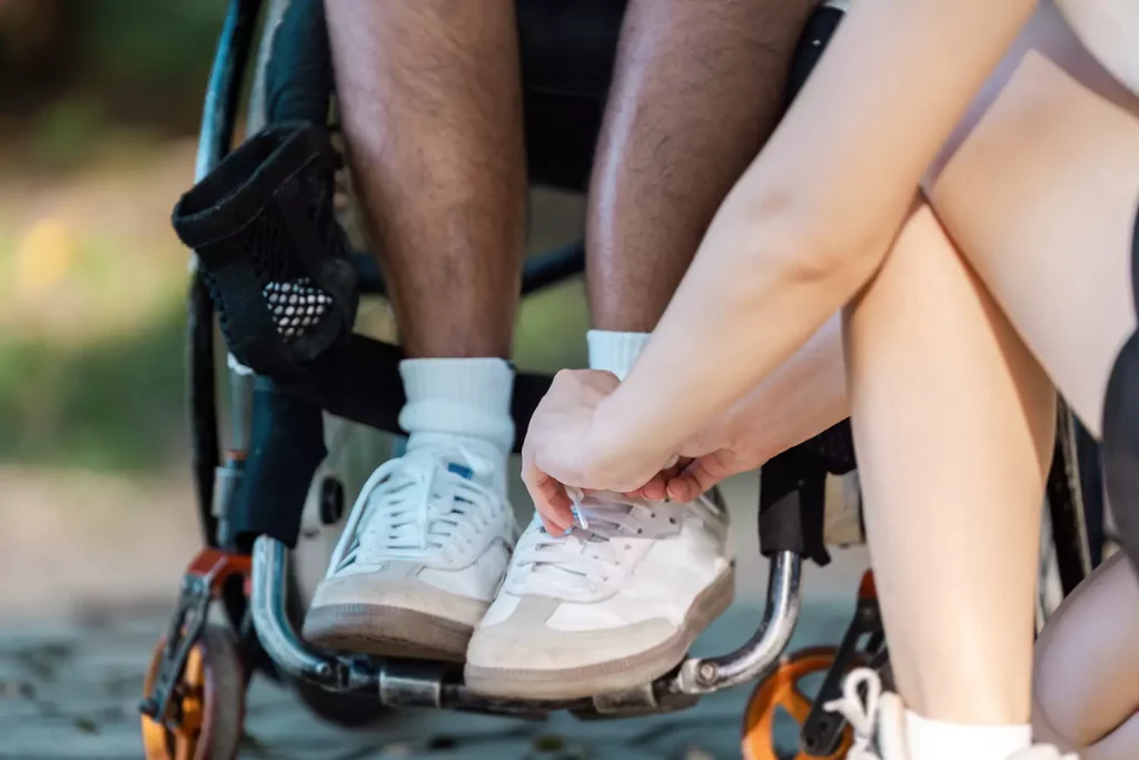 A disabled man sitting in his wheelchair and his support worker tying his shoes
